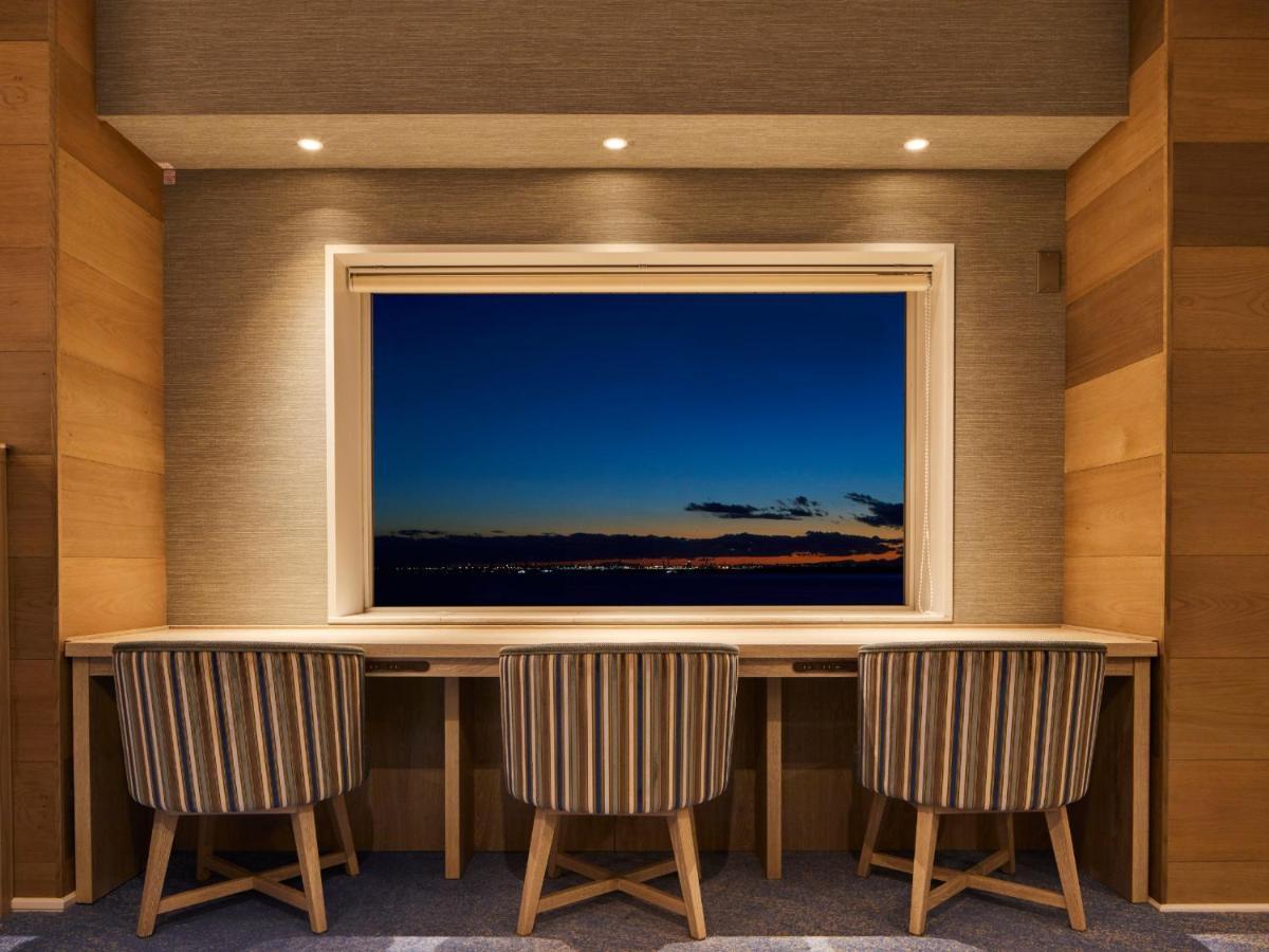 Grand Nikko Tokyo Bay Maihama Ξενοδοχείο Urayasu Εξωτερικό φωτογραφία The photo depicts a cozy workspace or study area featuring a long, minimalist desk with three chairs. The wall behind the desk is made of wood, creating a warm atmosphere. At the center, there is a large window that showcases a beautiful evening view