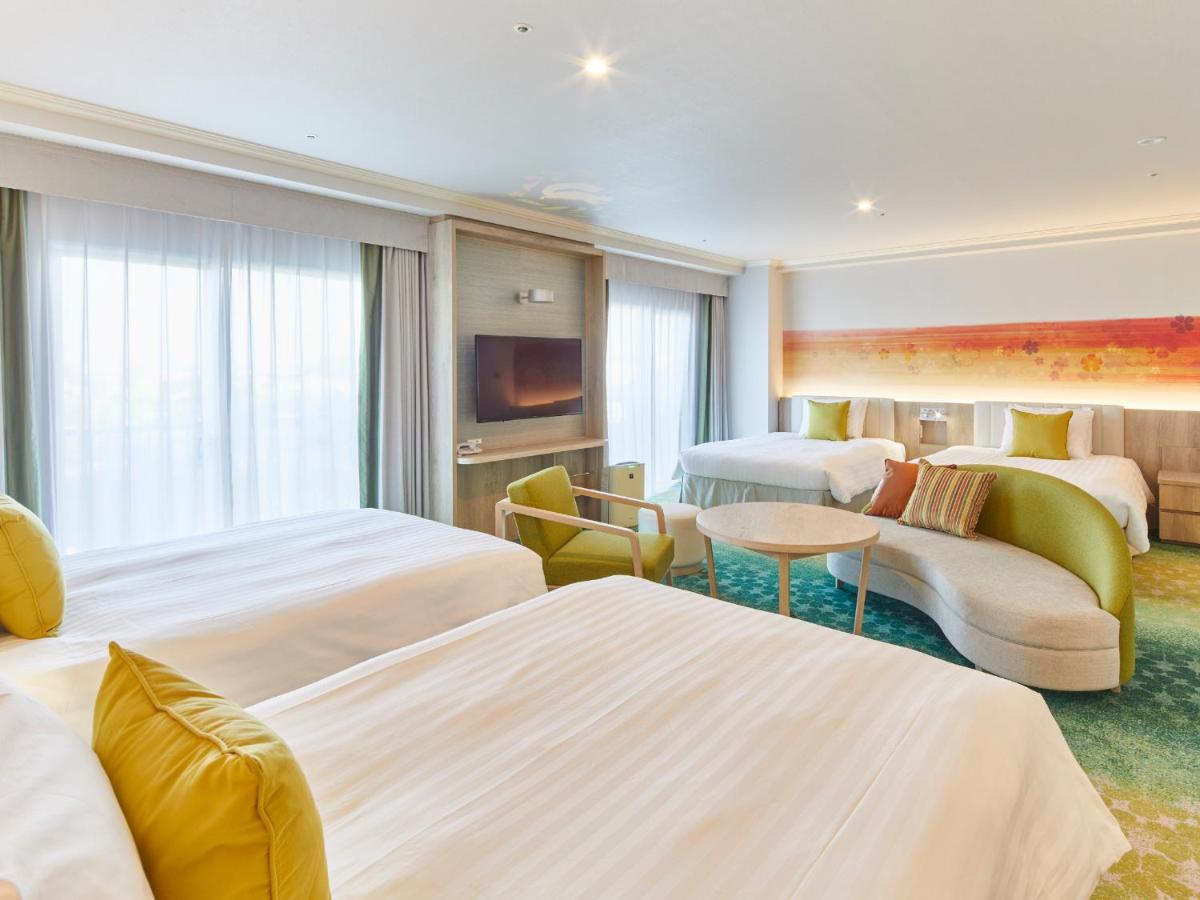 Grand Nikko Tokyo Bay Maihama Ξενοδοχείο Urayasu Εξωτερικό φωτογραφία The photo shows a modern hotel room that features two large beds covered with white bedding and decorative pillows. There is a contemporary, curved sofa in a light color, along with a round table in the middle. The room has large windows that allow n