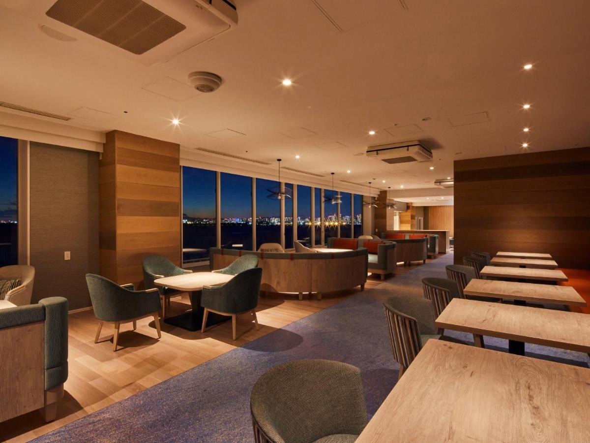Grand Nikko Tokyo Bay Maihama Ξενοδοχείο Urayasu Εξωτερικό φωτογραφία The photo shows a modern, well-lit lounge or café area. It features a mix of seating options, including cozy armchairs and tables with chairs. The space has large windows displaying a view, likely of a city or landscape at dusk, given the nighttime a