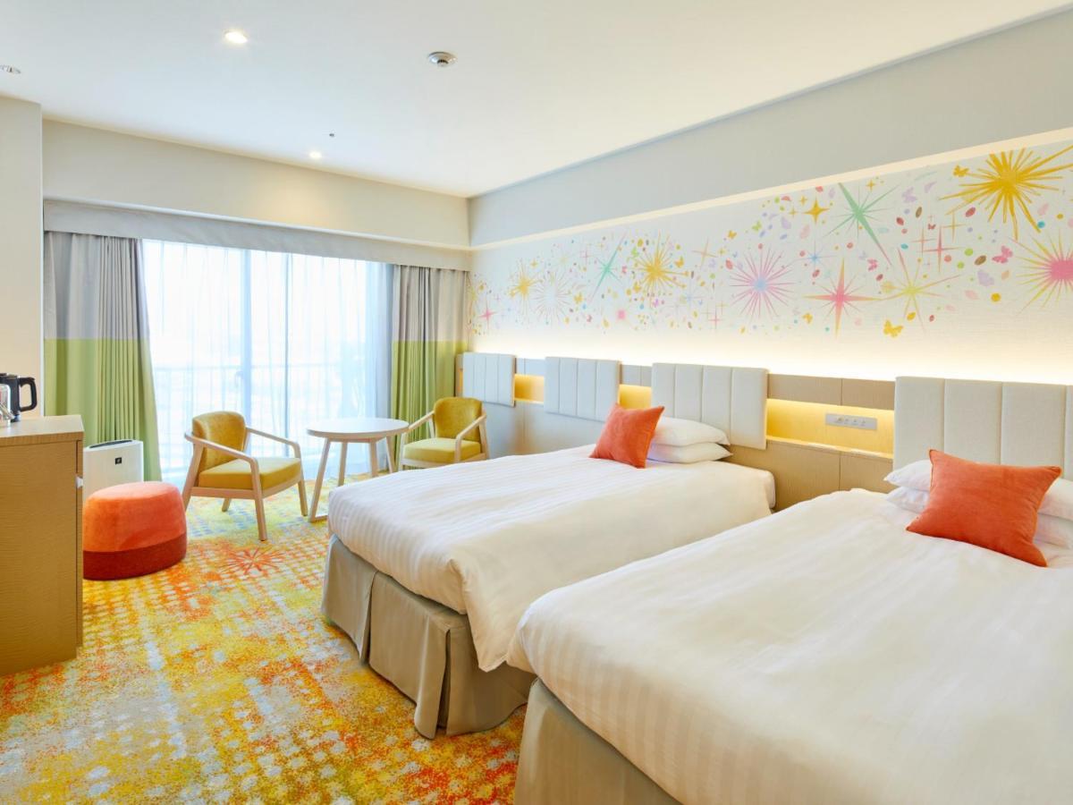 Grand Nikko Tokyo Bay Maihama Ξενοδοχείο Urayasu Εξωτερικό φωτογραφία The photo shows a modern hotel room featuring two twin beds with light-colored bedding and decorative orange cushions. There is a vibrant, colorful carpet on the floor, and the walls are adorned with playful designs, including bursts of color. A larg
