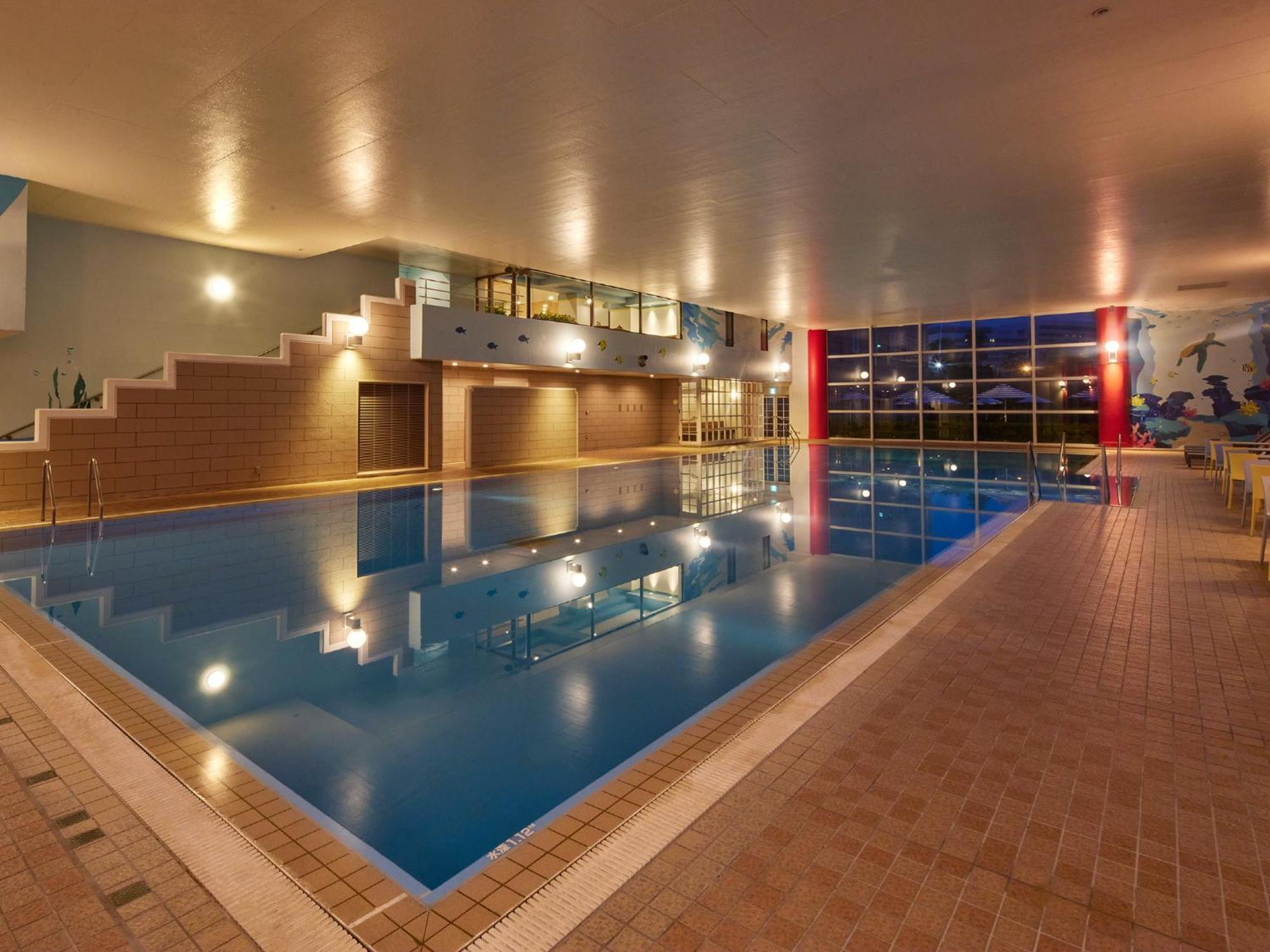 Grand Nikko Tokyo Bay Maihama Ξενοδοχείο Urayasu Εξωτερικό φωτογραφία The photo shows an indoor swimming pool area. The pool features a calm blue water surface and is surrounded by tiled flooring. There is a staircase leading to a higher level, likely providing access to a lounge or seating area. Large windows allow na