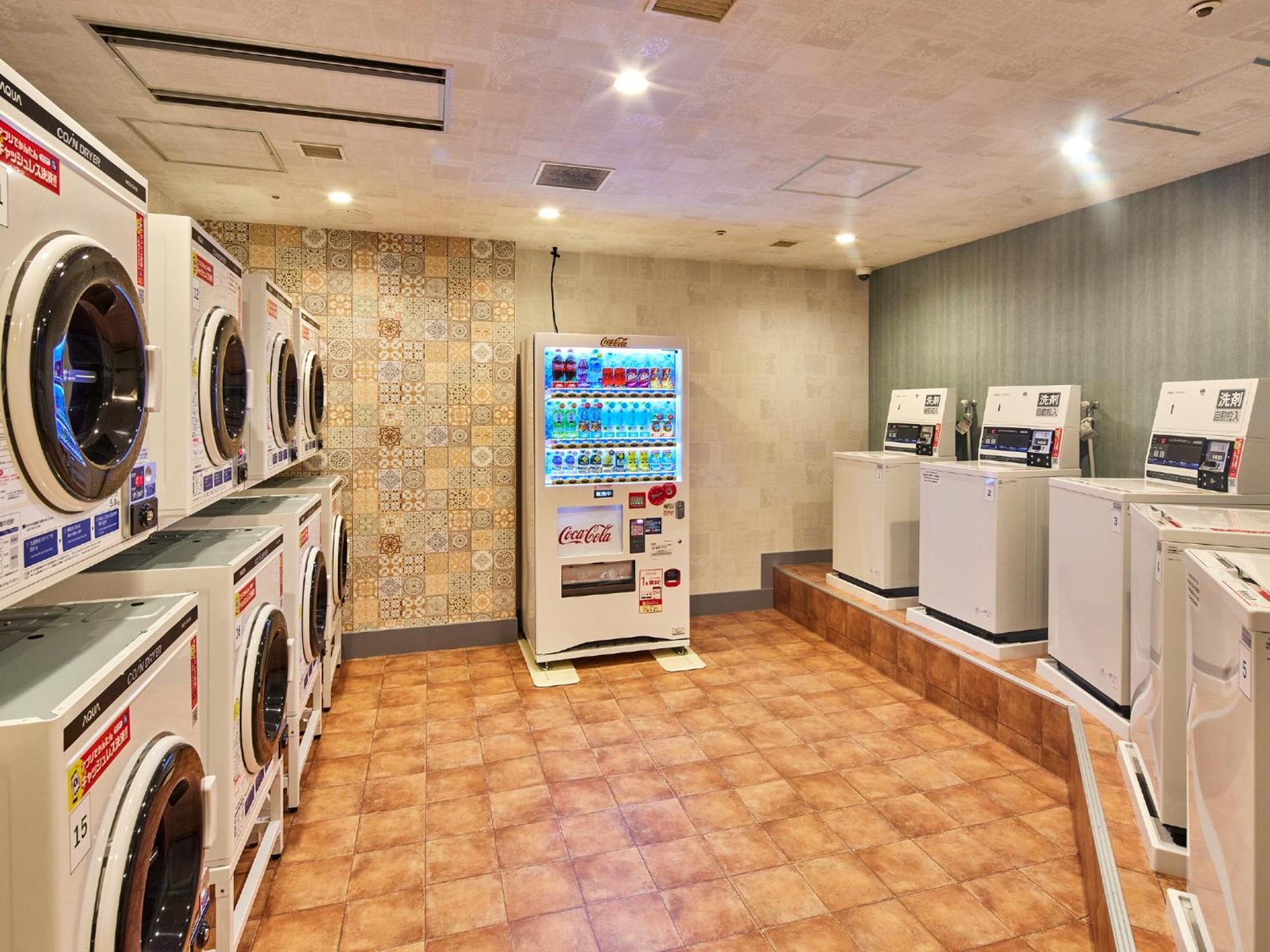 Grand Nikko Tokyo Bay Maihama Ξενοδοχείο Urayasu Εξωτερικό φωτογραφία The photo shows a laundry room equipped with several washing machines and dryers. On the left side, there are multiple front-loading washing machines arranged in a row, and on the right side, there are dryers. In the center, there is a vending machin