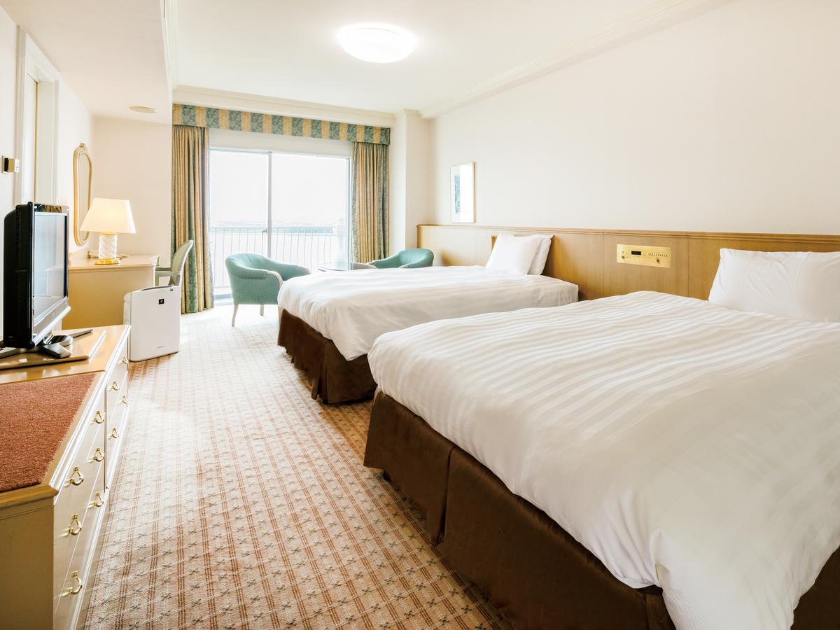 Grand Nikko Tokyo Bay Maihama Ξενοδοχείο Urayasu Εξωτερικό φωτογραφία The photo shows a hotel room featuring two large beds with white bedding and brown bases. There's a light-colored carpet on the floor, and the room is brightly lit. To one side, there is a television on a stand and a small white refrigerator. A desk 